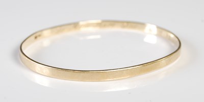 Lot 219 - A yellow metal oval bangle stamped "9CT",...