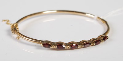 Lot 311 - A 9ct gold and garnet six stone hinged bangle,...